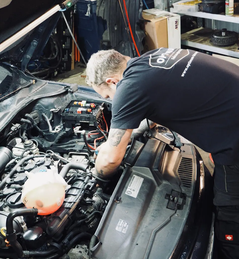 Mechaniker arbeitet an Batterie und Elektrik im offenen Motorraum eines Autos