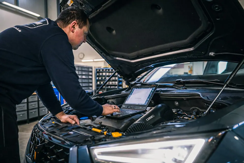 Technician with laptop diagnosing vehicle in workshop