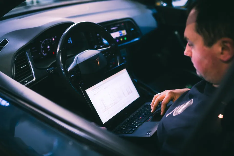 Technician working on vehicle diagnostics with laptop in car